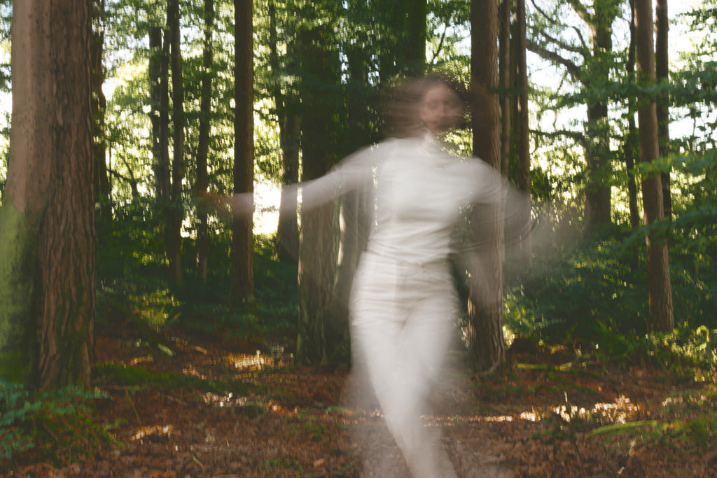 Kolorierte Aufnahme einer bewegten Figur zwischen hohen Bäumen im grünen Wald